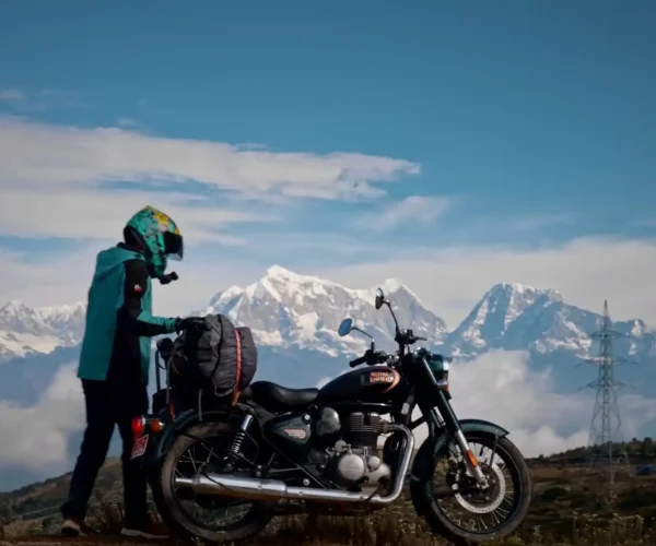 A motorcyclist stands beside a Royal Enfield bike, gazing at the breathtaking snow-capped peaks of the Annapurna and Dhaulagiri ranges during a motorbike tour in Nepal.